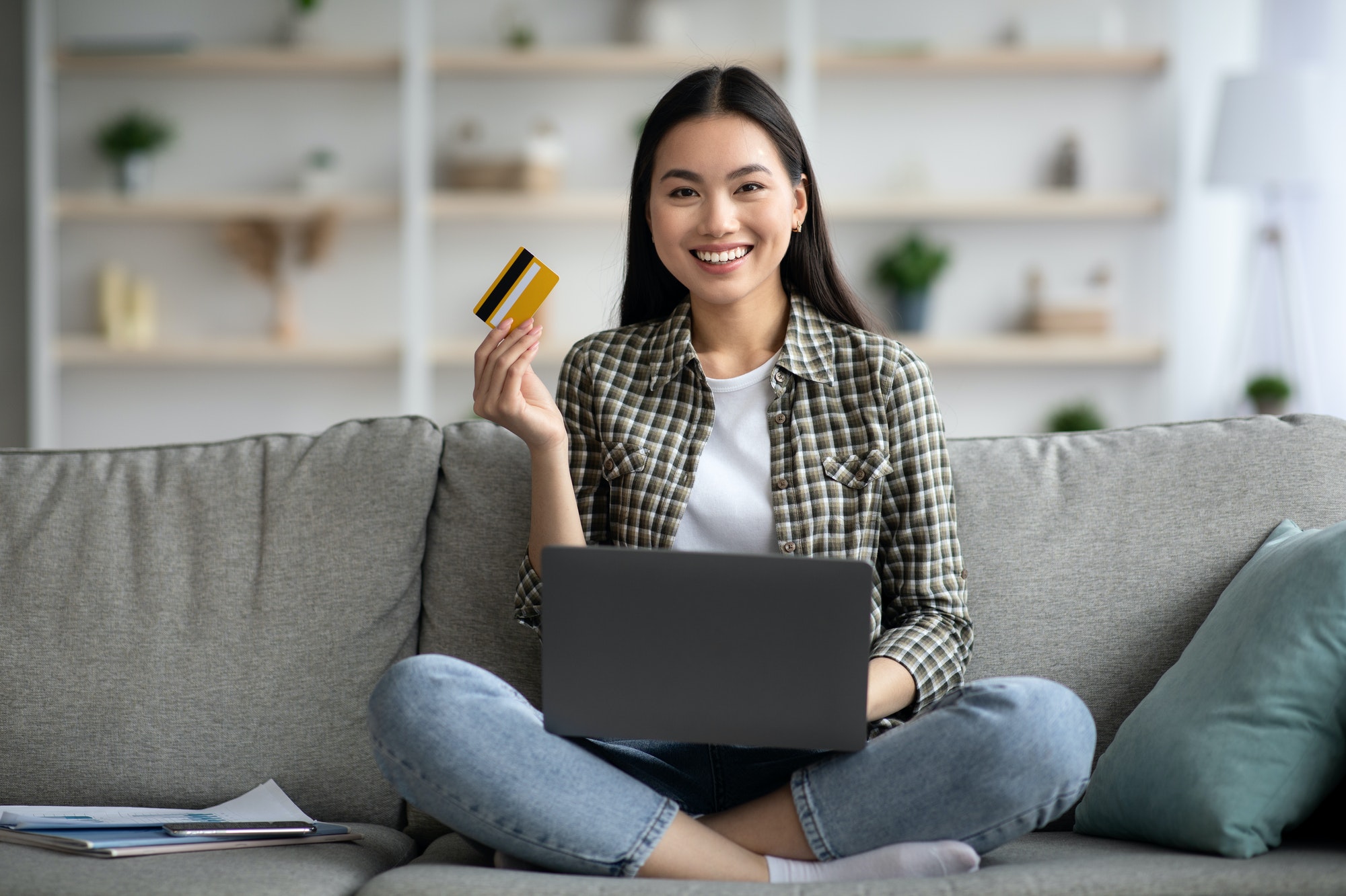 Happy woman using laptop and credit card at home
